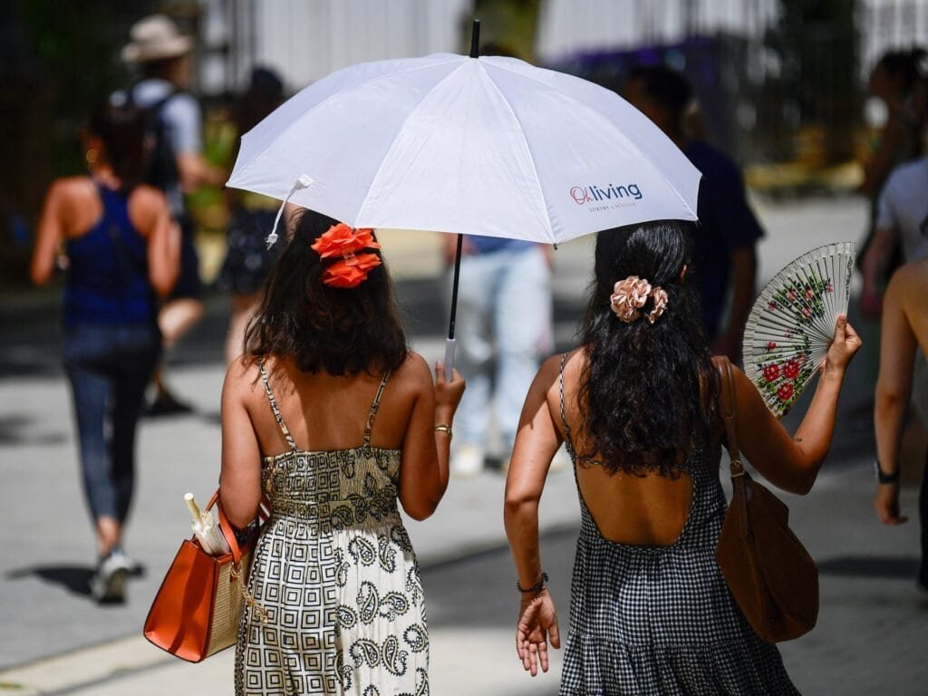 Two women walk down the street with an umbrella because of high heat in Southern Europe